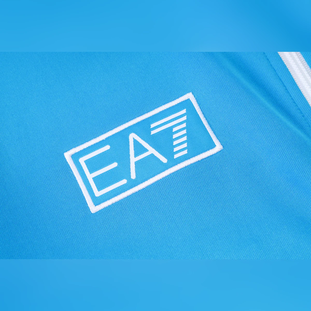 Chándal Napoli Celeste con V Blanca y Azul 2025/26 – detalle del logotipo EA7