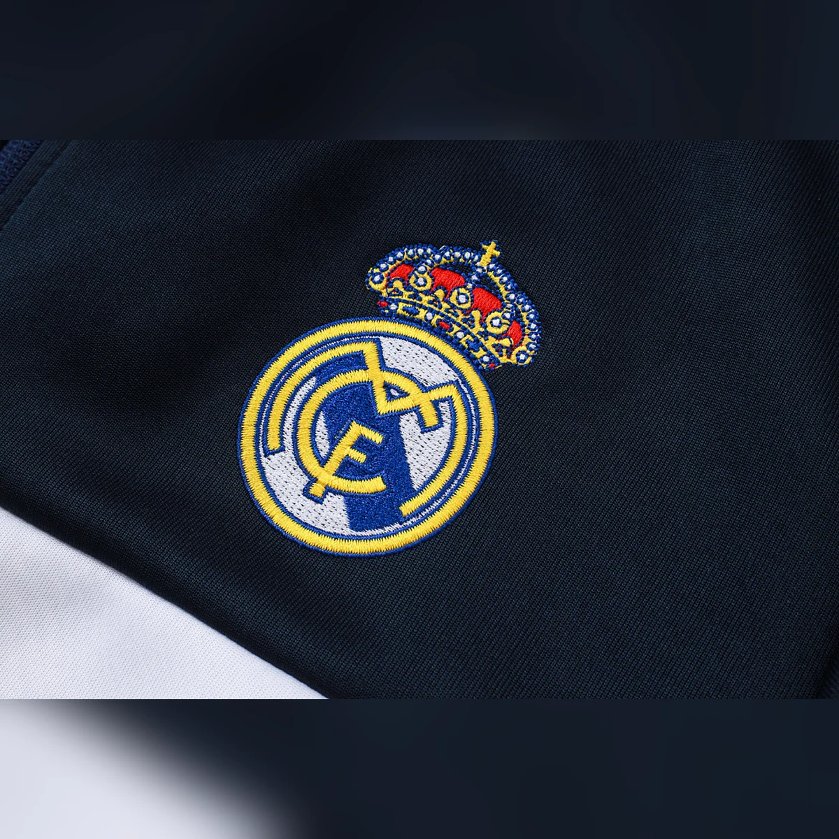Chándal Real Madrid Azul Marino Franja Blanca 2026/27 – detalle del escudo